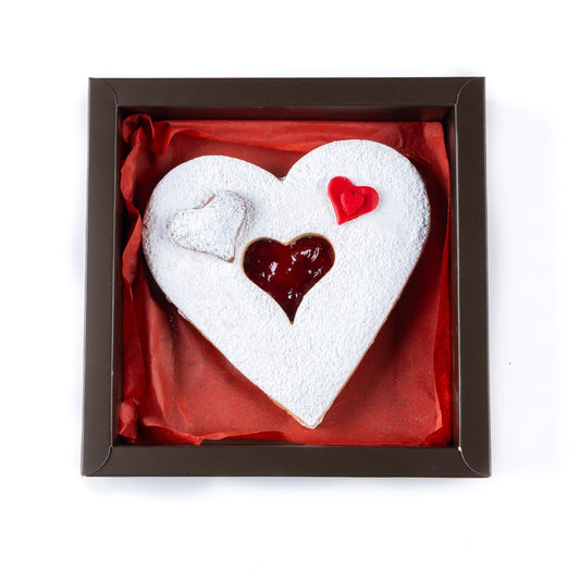 Heart-shaped cookie with white frosting and red heart design in a box on a white background