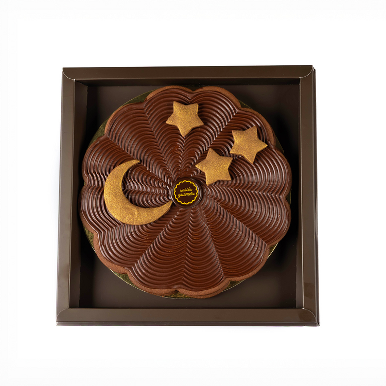 Chocolate cake with gold decorations in a brown box on a white background